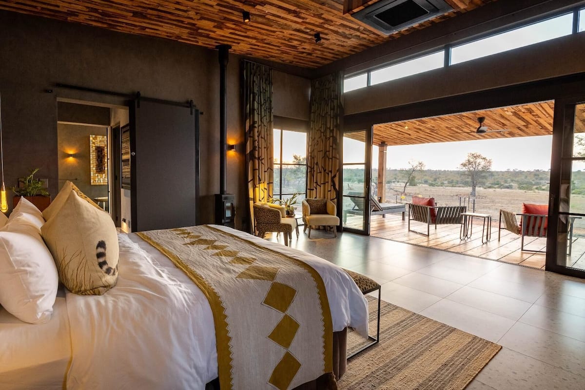 Un dormitorio espacioso con una cama grande, vistas al exterior y un balcón con mobiliario.