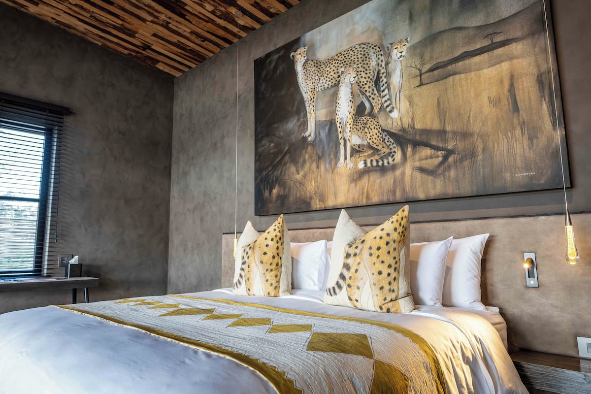 Un dormitorio con un cuadro grande de chitas, una cama con ropa de cama estampada y una lámpara moderna.