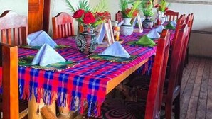 A wooden dining table with chairs, a colorful tablecloth, and potted plants. - Bwindi Neckview Lodge (Bwindi)