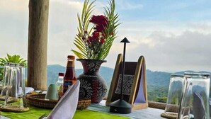A table set outdoors with a view of mountains, a thatched roof, and a decorative vase. - Bwindi Neckview Lodge (Bwindi)