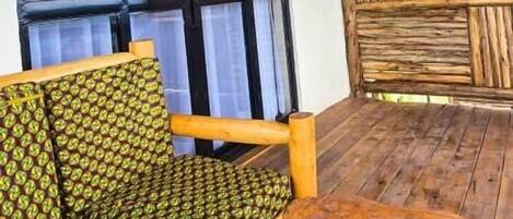 Um banco de madeira e um sofá com capa estampada numa varanda com parede de madeira e janelas com cortinas.