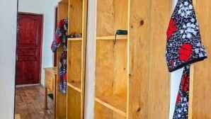 A room with a wooden wardrobe, a mirror, a wooden desk, and a red door. - Bwindi Neckview Lodge (Bwindi)