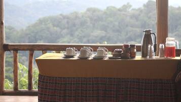 Una mesa con juegos de té y una cafetera, con vista a una cadena montañosa boscosa.