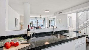 A modern kitchen with a black countertop, stainless steel sink, and a view of the beach through large windows. - Solaga - Miguel (Málaga)