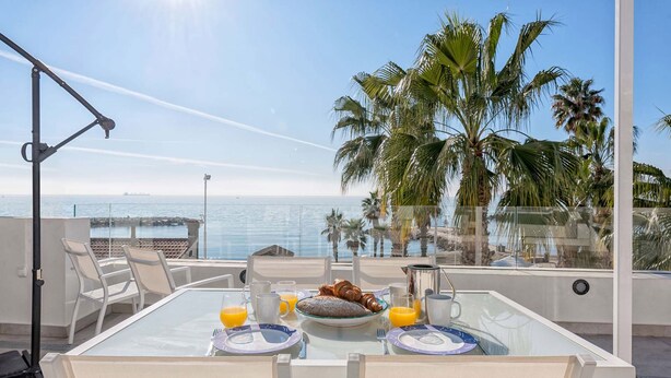 A dining table with chairs and breakfast items, overlooking a beach and palm trees. - Solaga - Miguel (Málaga)