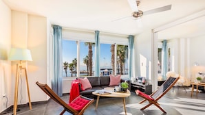 A modern living room with a sofa, two lounge chairs, a coffee table, and a view of palm trees and the sea. - Solaga - Miguel (Málaga)