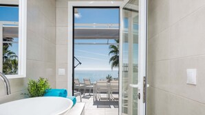 A bathroom with a large white sink, a glass shower door, and a view of the ocean through the door. - Solaga - Miguel (Málaga)