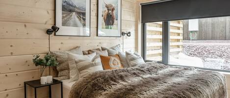 A cozy bedroom with a large bed, wooden walls, framed pictures, and a view of the outdoors.