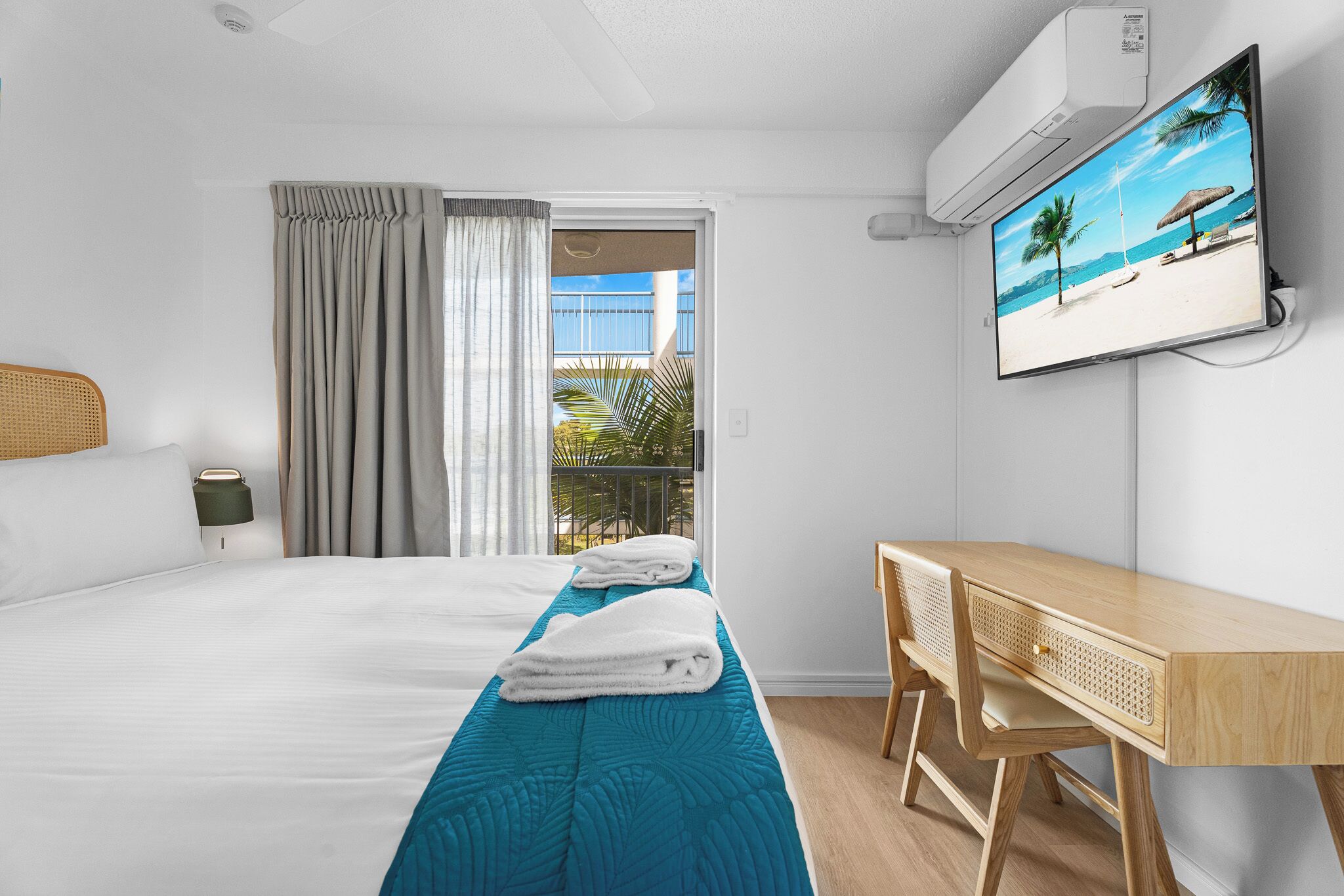 Hotellihuone, jossa on sänky, työpöytä, televisio ja näkymä rannalle.