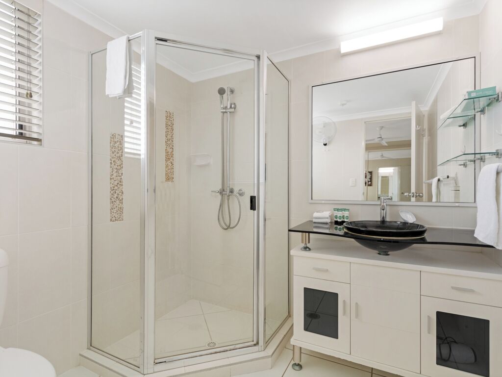 A modern bathroom with a glass-enclosed shower, a white sink with a black basin, and a large mirror above the sink.