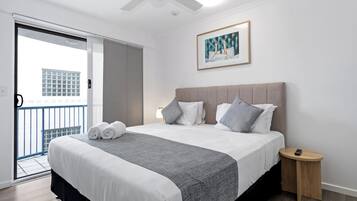 A hotel room with a bed, a bedside table, a ceiling fan, a framed picture on the wall, and a balcony door.