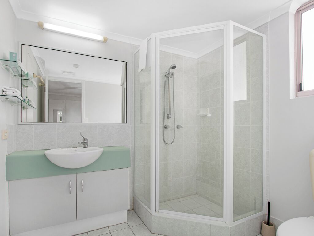 Uma casa de banho moderna com lavatório branco, bancada verde e cabine de duche envidraçada.