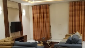 A modern living room with a flat-screen TV, two sofas, a coffee table, and a dining table. - Favour home (Abuja)