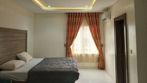 A bedroom with a bed, a headboard, a window with curtains, and an air conditioning unit. - Favour home (Abuja)