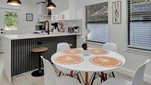 A modern kitchen with a central island, pendant lighting, and a dining area with a round table and chairs. - Family Fun Backyard Oasis Hot Tub Games BBQ (St. Petersburg)