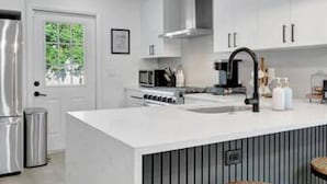 A modern kitchen with white cabinetry, a central island with a sink, and two pendant lights. - Family Fun Backyard Oasis Hot Tub Games BBQ (St. Petersburg)
