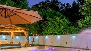 A swimming pool with a covered seating area and a white wall with lights. - Family Fun Backyard Oasis Hot Tub Games BBQ (St. Petersburg)