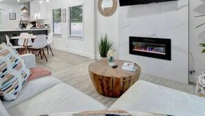A modern living room with a flat-screen TV mounted on the wall, a fireplace, and a round wooden coffee table. - Family Fun Backyard Oasis Hot Tub Games BBQ (St. Petersburg)