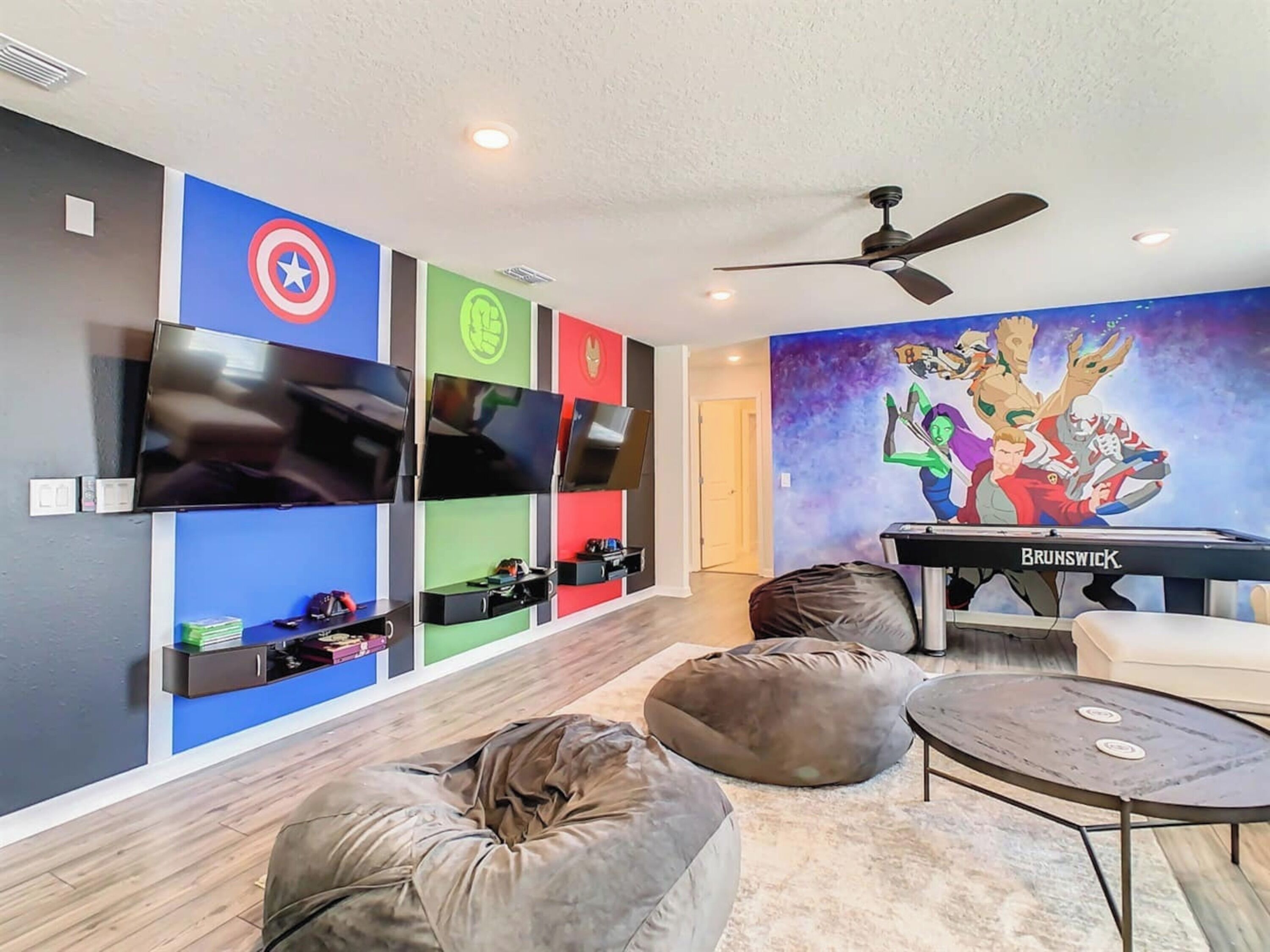 A modern living room with a flat-screen TV, a pool table, bean bags, and a vibrant mural.