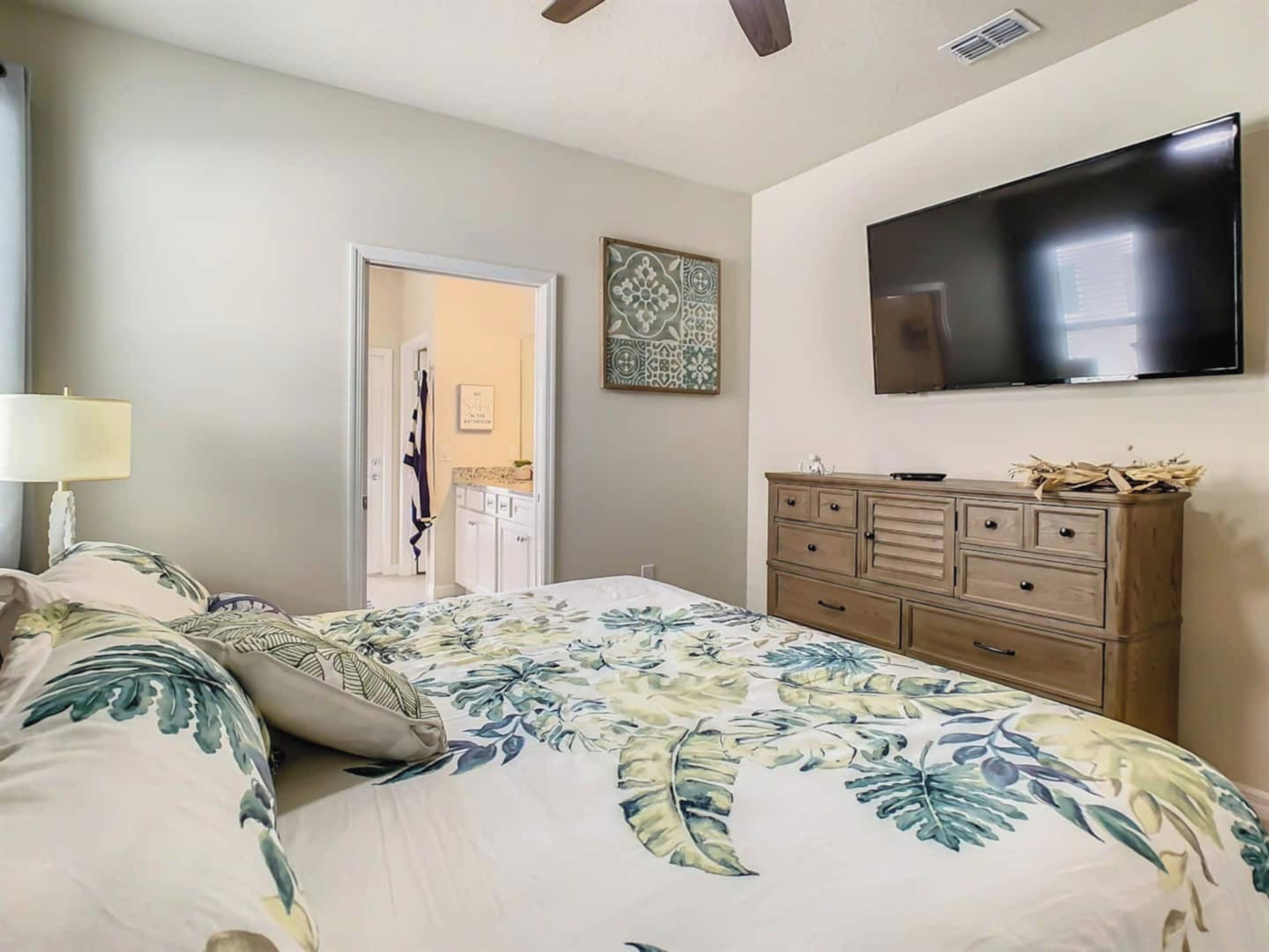 A bedroom with a bed, a dresser, a television mounted on the wall, and a door leading to another room.