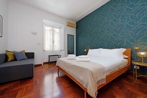 Une chambre à coucher avec un lit, un canapé, une fenêtre et un mur orné d’un motif de feuilles.