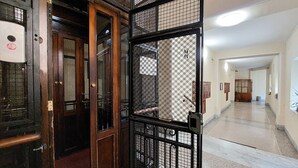 Un corridoio con una porta in legno e un cancello in metallo, che conduce a una stanza con pavimento piastrellato e parete bianca.