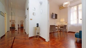 Un'ampia zona giorno con pavimento in legno, un tavolo da pranzo con sedie, una TV a parete e una poltrona blu.