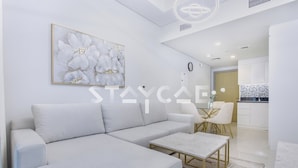 Ein modernes Wohnzimmer mit einem hellgrauen Sofa, einem Couchtisch und einem Essbereich mit einem Glastisch und weißen Stühlen.
