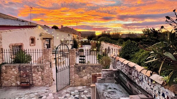 A courtyard with stone walls, a gate, and a building with a tiled roof.