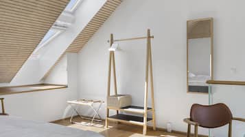 Ein modernes Schlafzimmer mit schrägen Wänden, einem Bettgestell aus Holz, einem Nachttisch, einem Sessel, einer Pendelleuchte und einem großen Spiegel.