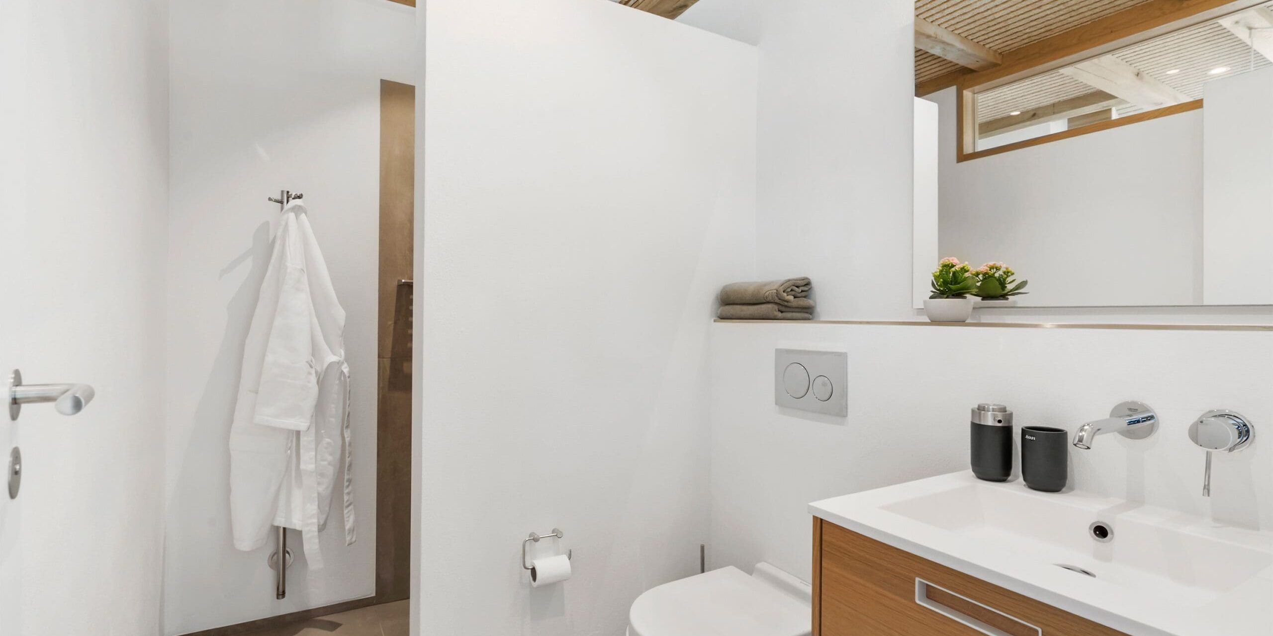 A modern bathroom with a white sink, two black cups, a towel rack, and a potted plant.