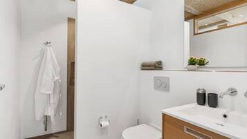 A modern bathroom with a white sink, two black cups, a towel rack, and a potted plant.