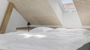 A bedroom with a sloped ceiling, a skylight, a bed with white bedding, and a bedside table with a lamp.