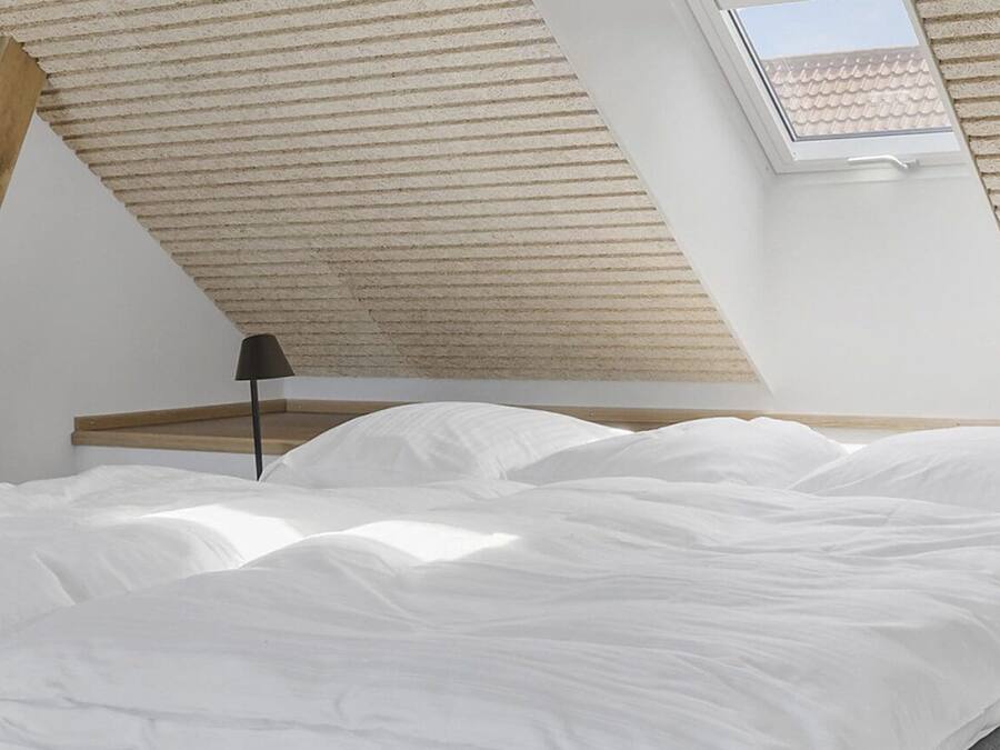 A bedroom with a sloped ceiling, a skylight, a bed with white bedding, and a bedside table with a lamp.