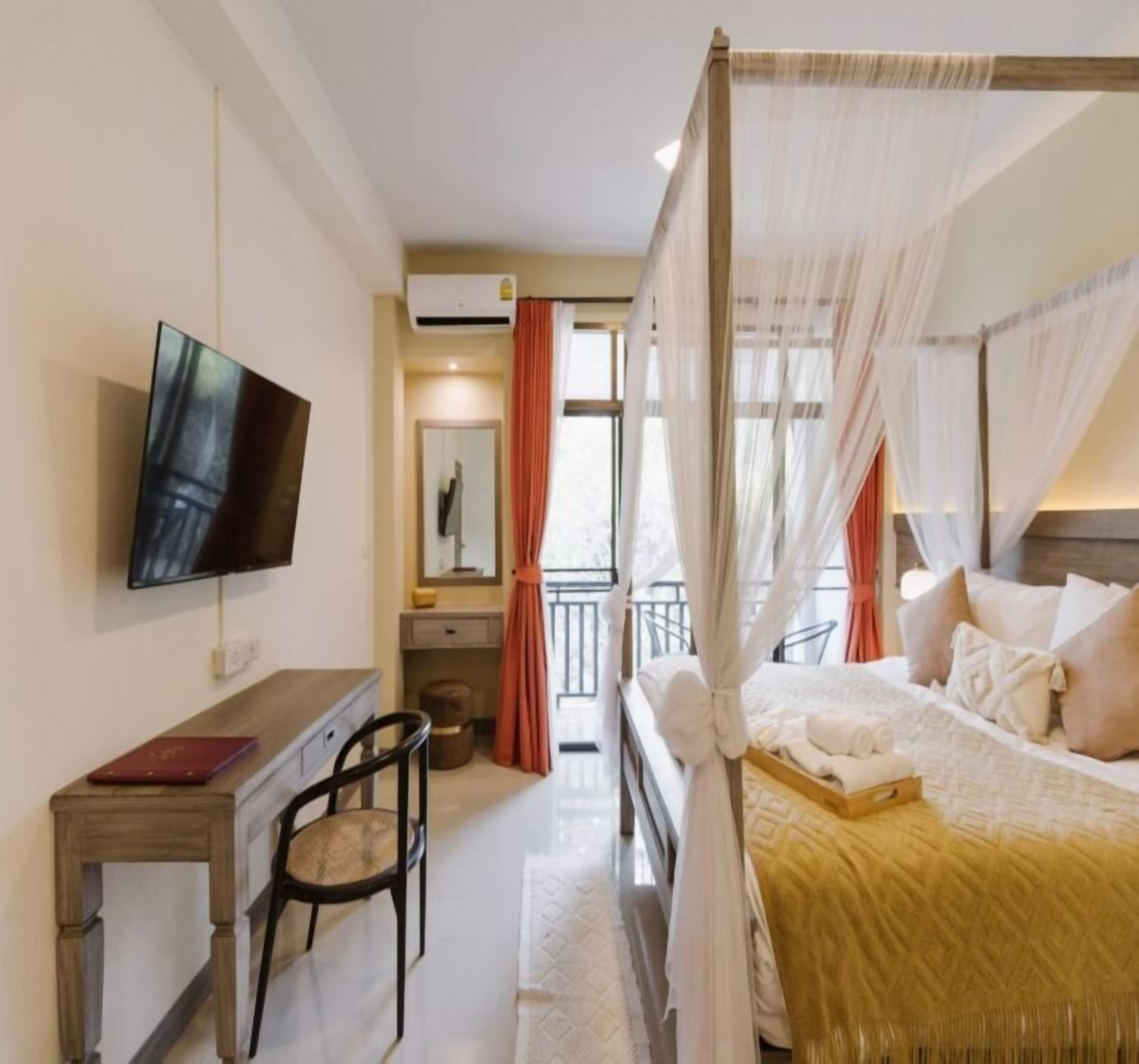Een hotelkamer met een hemelbed, een bureau met een stoel, een televisietoestel en een balkon met rode gordijnen.