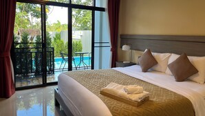 A hotel room with a large bed, a bedside table with a lamp, and a view of a swimming pool through large windows. - Radateeree Boutique Resort (Chiang Mai)