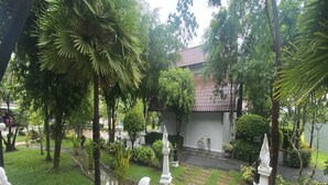 A garden with a paved walkway, palm trees, and a building with a tiled roof. - Radateeree Boutique Resort (Chiang Mai)