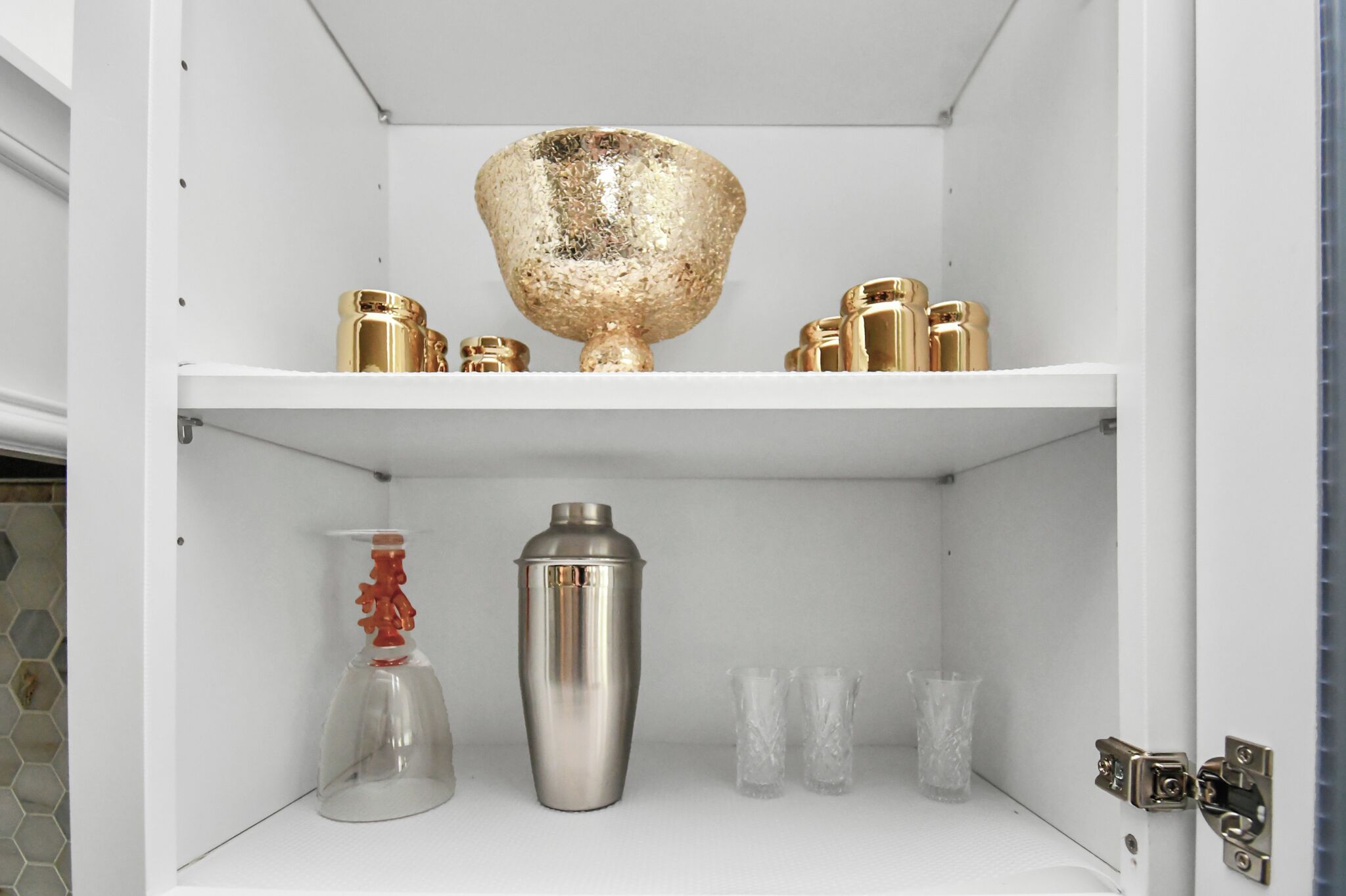 A white cabinet with shelves containing various glassware and metal containers.