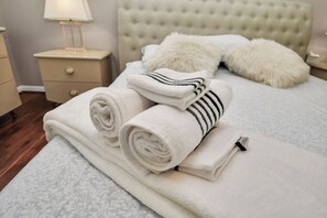 Una cama bien hecha con toallas blancas y a rayas, un cabecero capitonado y una mesita de noche con una lámpara.
