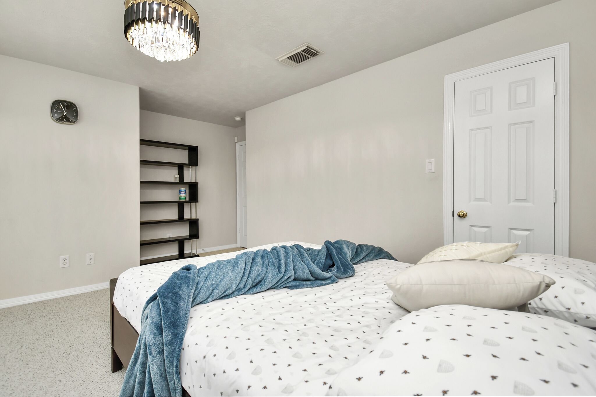 Una camera da letto con un letto, un lampadario, una porta e una sveglia a muro.