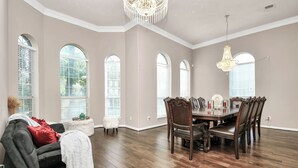 A spacious dining area with a wooden table and chairs, large windows with blinds, and a chandelier. - REIGN Mini-mansion (Houston)