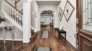 A spacious hallway with a wooden staircase, a bench, and a rug leading to a dining area. - REIGN Mini-mansion (Houston)