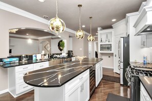 Une cuisine moderne dotée d’un grand îlot central, d’appareils électroménagers en acier inoxydable et de luminaires suspendus.