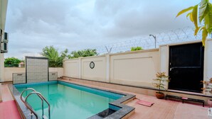 A swimming pool with a tiled deck, a metal ladder, and a bench. - VIBE 2.0 (Jaipur)