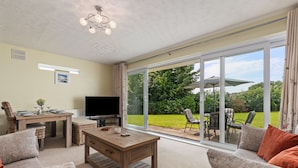 A spacious living room with a wooden coffee table, a flat-screen TV, and a dining area with a table and chairs. - Harbour Reach - Close to Beach Parking (Saundersfoot)