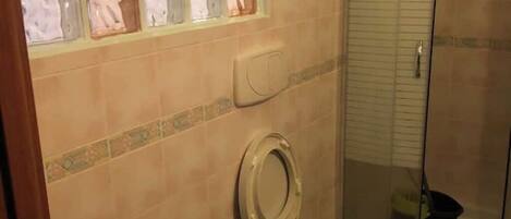 Ein Badezimmer mit Toilette, Duschkabine und Fenster mit satinierten Glasfeldern.