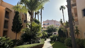 A courtyard with a paved pathway, palm trees, and a building with balconies. - Seaview Apartment Estrela da Luz, Praia da Luz (Lagos)