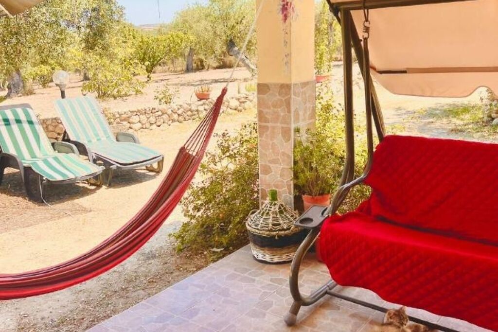 Een terras met twee gestreepte loungestoelen, een rode bank en een hangmat.