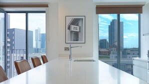 Una cocina moderna con una isla grande, un lavaplatos integrado y vistas a un paisaje urbano a través de amplios ventanales.