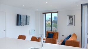 Una cocina moderna con una isla grande, un lavamanos integrado y una zona de estar con sillas naranjas y un sofá.